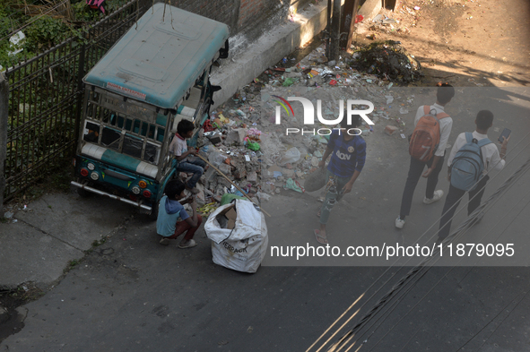 Two young child laborers collect plastic bottles and other reusable items from a roadside garbage disposal area while a worker and two schoo...