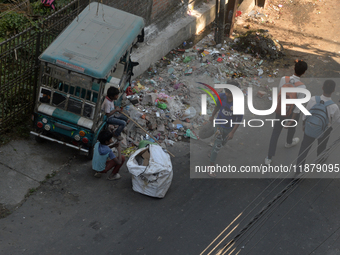 Two young child laborers collect plastic bottles and other reusable items from a roadside garbage disposal area while a worker and two schoo...