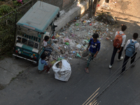 Two young child laborers collect plastic bottles and other reusable items from a roadside garbage disposal area while a worker and two schoo...