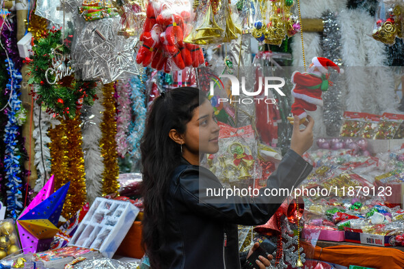 A lady shops for a Santa Claus doll, and a mother and child check out Christmas trees at a marketplace ahead of Christmas in Kolkata, India,...