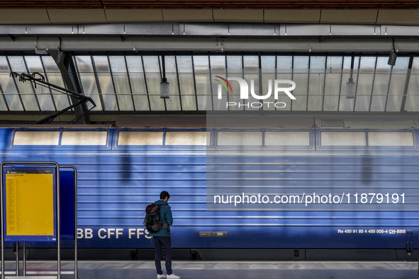 A passenger waits beside a stationary blue Swiss Federal Railways (SBB CFF FFS) train at Zurich Station in Zurich, Switzerland, on March 29,...