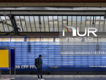 A passenger waits beside a stationary blue Swiss Federal Railways (SBB CFF FFS) train at Zurich Station in Zurich, Switzerland, on March 29,...