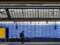 A passenger waits beside a stationary blue Swiss Federal Railways (SBB CFF FFS) train at Zurich Station in Zurich, Switzerland, on March 29,...