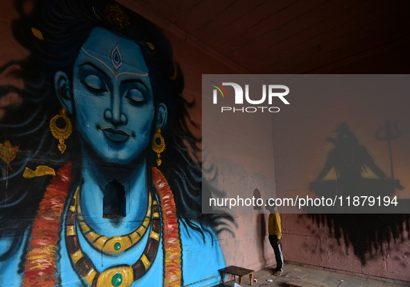 A man stands next to a mural painting of Lord Shiva on the wall of a temple, created as part of the ongoing 'Paint My City' project for the...