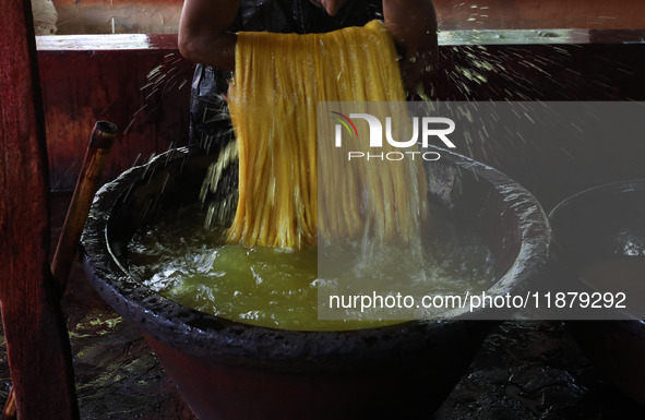 A weaver removes water from threads after coloring them, before they dry, for making a saree, a traditional cloth used for women's clothing,...