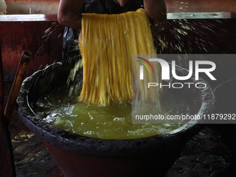 A weaver removes water from threads after coloring them, before they dry, for making a saree, a traditional cloth used for women's clothing,...