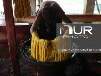 A weaver removes water from threads after coloring them, before they dry, for making a saree, a traditional cloth used for women's clothing,...