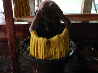 A weaver removes water from threads after coloring them, before they dry, for making a saree, a traditional cloth used for women's clothing,...