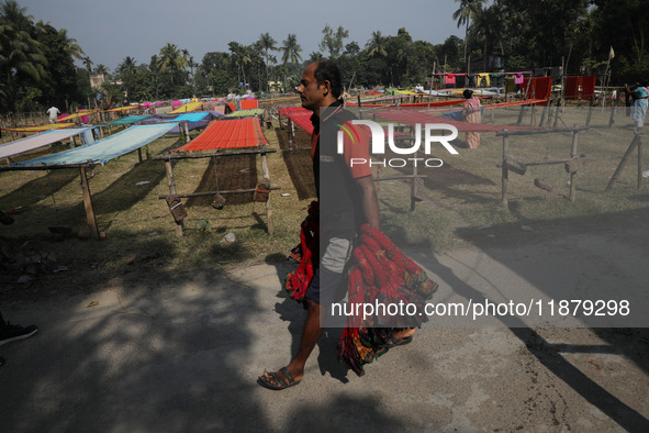 A weaver carries sarees, a traditional cloth used for women's clothing, to hang out to dry after weaving them at a workshop in Santipur, Ind...