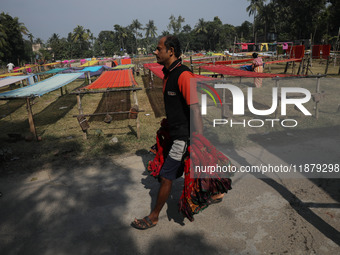 A weaver carries sarees, a traditional cloth used for women's clothing, to hang out to dry after weaving them at a workshop in Santipur, Ind...