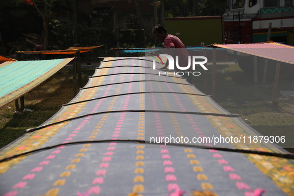 A weaver arranges a saree, a traditional cloth used for women's clothing, as it hangs out to dry after weaving it at a workshop in Santipur...