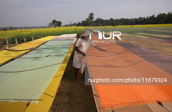 A weaver arranges a saree, a traditional cloth used for women's clothing, as it hangs out to dry after weaving it at a workshop in Santipur...