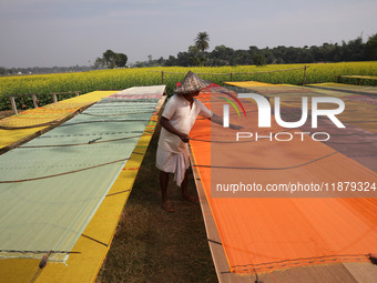 A weaver arranges a saree, a traditional cloth used for women's clothing, as it hangs out to dry after weaving it at a workshop in Santipur...