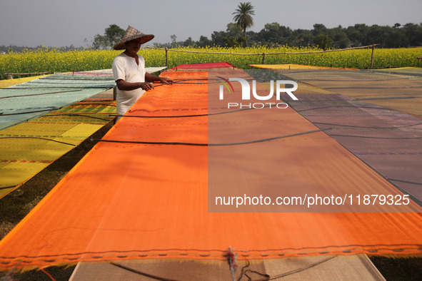 A weaver arranges a saree, a traditional cloth used for women's clothing, as it hangs out to dry after weaving it at a workshop in Santipur...