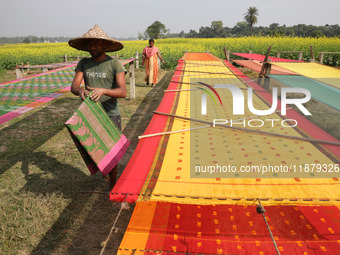 A weaver arranges a saree, a traditional cloth used for women's clothing, as it hangs out to dry after weaving it at a workshop in Santipur...