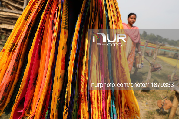 A weaver walks past sarees, a traditional cloth used for women's clothing, as they hang out to dry after weaving at a workshop in Santipur t...