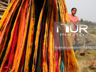 A weaver walks past sarees, a traditional cloth used for women's clothing, as they hang out to dry after weaving at a workshop in Santipur t...