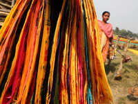 A weaver walks past sarees, a traditional cloth used for women's clothing, as they hang out to dry after weaving at a workshop in Santipur t...