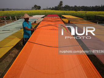 A weaver arranges a saree, a traditional cloth used for women's clothing, as it hangs out to dry after weaving it at a workshop in Santipur...