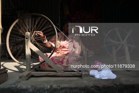 A woman weaves cotton yarn using a traditional thread machine at a handloom saree manufacturing unit before making sarees, a traditional clo...