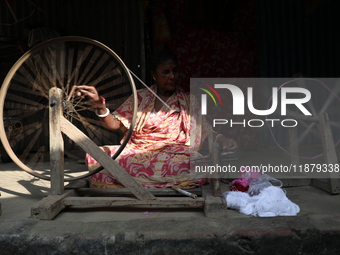 A woman weaves cotton yarn using a traditional thread machine at a handloom saree manufacturing unit before making sarees, a traditional clo...