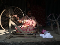 A woman weaves cotton yarn using a traditional thread machine at a handloom saree manufacturing unit before making sarees, a traditional clo...