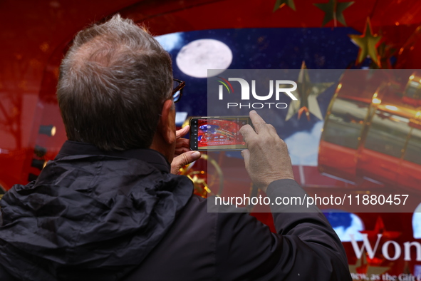 People take photos with their mobile devices of Macy's department store windows in New York, N.Y., on December 17, 2024. 