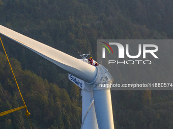 Workers lift the blades of a wind turbine at the construction site of the Guishushan Wind Farm project in Qingyun town of Congjiang county,...