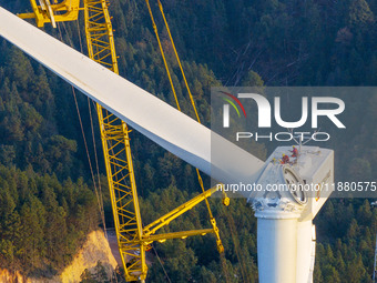 Workers lift the blades of a wind turbine at the construction site of the Guishushan Wind Farm project in Qingyun town of Congjiang county,...