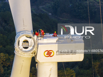 Workers lift the blades of a wind turbine at the construction site of the Guishushan Wind Farm project in Qingyun town of Congjiang county,...