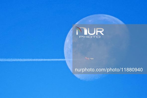 A passenger plane flies past the moon in Yantai, China, on December 19, 2024. 