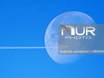 A passenger plane flies past the moon in Yantai, China, on December 19, 2024. (