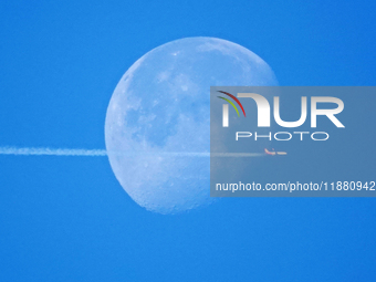 A passenger plane flies past the moon in Yantai, China, on December 19, 2024. (