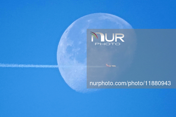 A passenger plane flies past the moon in Yantai, China, on December 19, 2024. 