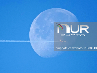 A passenger plane flies past the moon in Yantai, China, on December 19, 2024. (