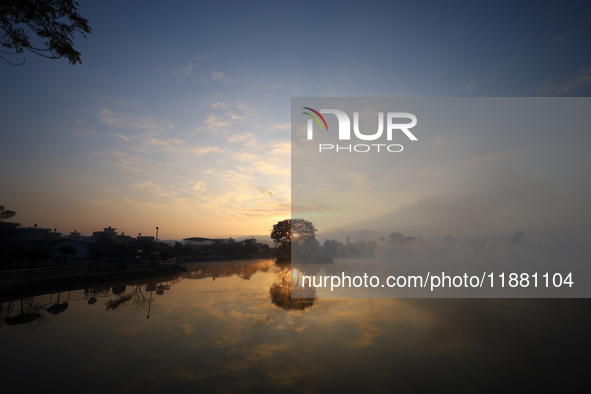 The sun rises against a tree that stands in the middle of the Taudaha wetland on the outskirts of Kathmandu, Nepal, on December 19, 2024. 