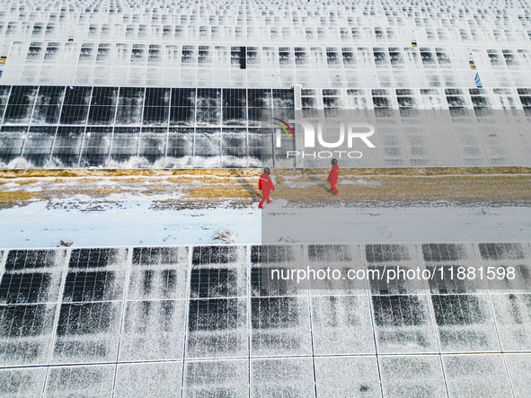 Operation and maintenance personnel clean snow on photovoltaic modules in the 100,000-kilowatt photovoltaic power generation project area of...