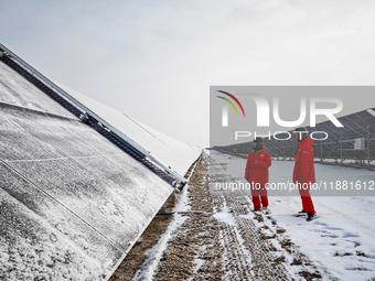 Operation and maintenance personnel clean snow on photovoltaic modules in the 100,000-kilowatt photovoltaic power generation project area of...