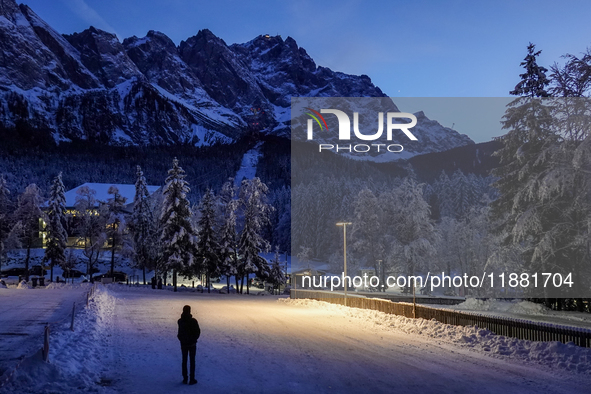 A person stands silhouetted against the illuminated snowy Alps on a winter evening in Grainau, Garmisch-Partenkirchen, Bavaria, Germany, on...