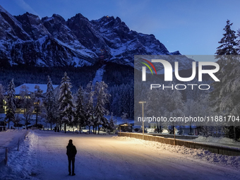 A person stands silhouetted against the illuminated snowy Alps on a winter evening in Grainau, Garmisch-Partenkirchen, Bavaria, Germany, on...