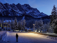 A person stands silhouetted against the illuminated snowy Alps on a winter evening in Grainau, Garmisch-Partenkirchen, Bavaria, Germany, on...