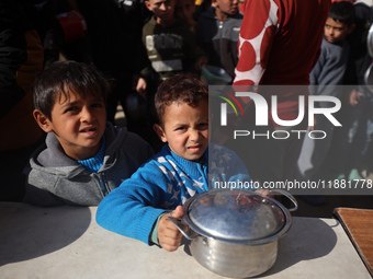 Palestinians gather to receive food cooked by a charity kitchen amid a hunger crisis as the Israel-Gaza conflict continues in Deir el-Balah,...