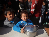 Palestinians gather to receive food cooked by a charity kitchen amid a hunger crisis as the Israel-Gaza conflict continues in Deir el-Balah,...