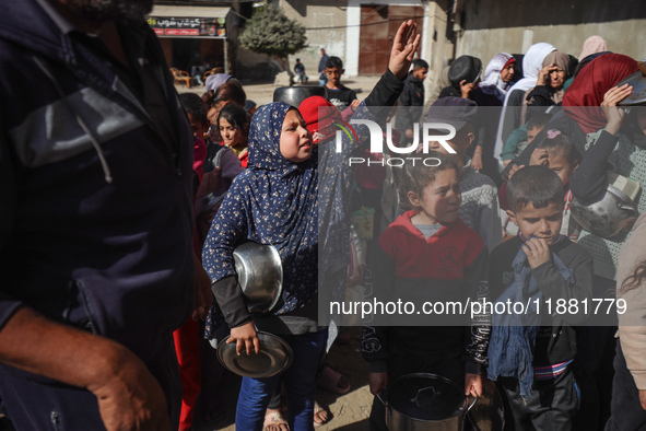 Palestinians gather to receive food cooked by a charity kitchen amid a hunger crisis as the Israel-Gaza conflict continues in Deir el-Balah,...