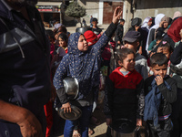 Palestinians gather to receive food cooked by a charity kitchen amid a hunger crisis as the Israel-Gaza conflict continues in Deir el-Balah,...