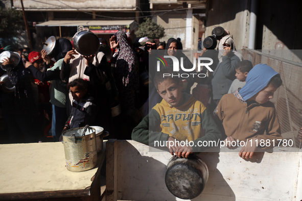 Palestinians gather to receive food cooked by a charity kitchen amid a hunger crisis as the Israel-Gaza conflict continues in Deir el-Balah,...