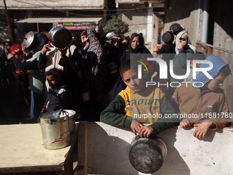 Palestinians gather to receive food cooked by a charity kitchen amid a hunger crisis as the Israel-Gaza conflict continues in Deir el-Balah,...