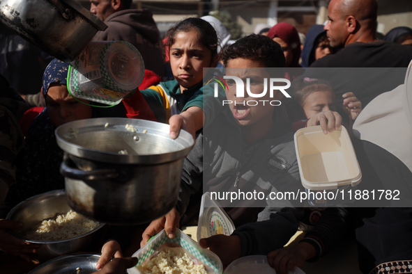 Palestinians gather to receive food cooked by a charity kitchen amid a hunger crisis as the Israel-Gaza conflict continues in Deir el-Balah,...