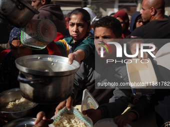 Palestinians gather to receive food cooked by a charity kitchen amid a hunger crisis as the Israel-Gaza conflict continues in Deir el-Balah,...