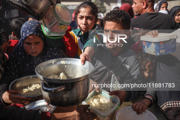 Palestinians gather to receive food cooked by a charity kitchen amid a hunger crisis as the Israel-Gaza conflict continues in Deir el-Balah,...